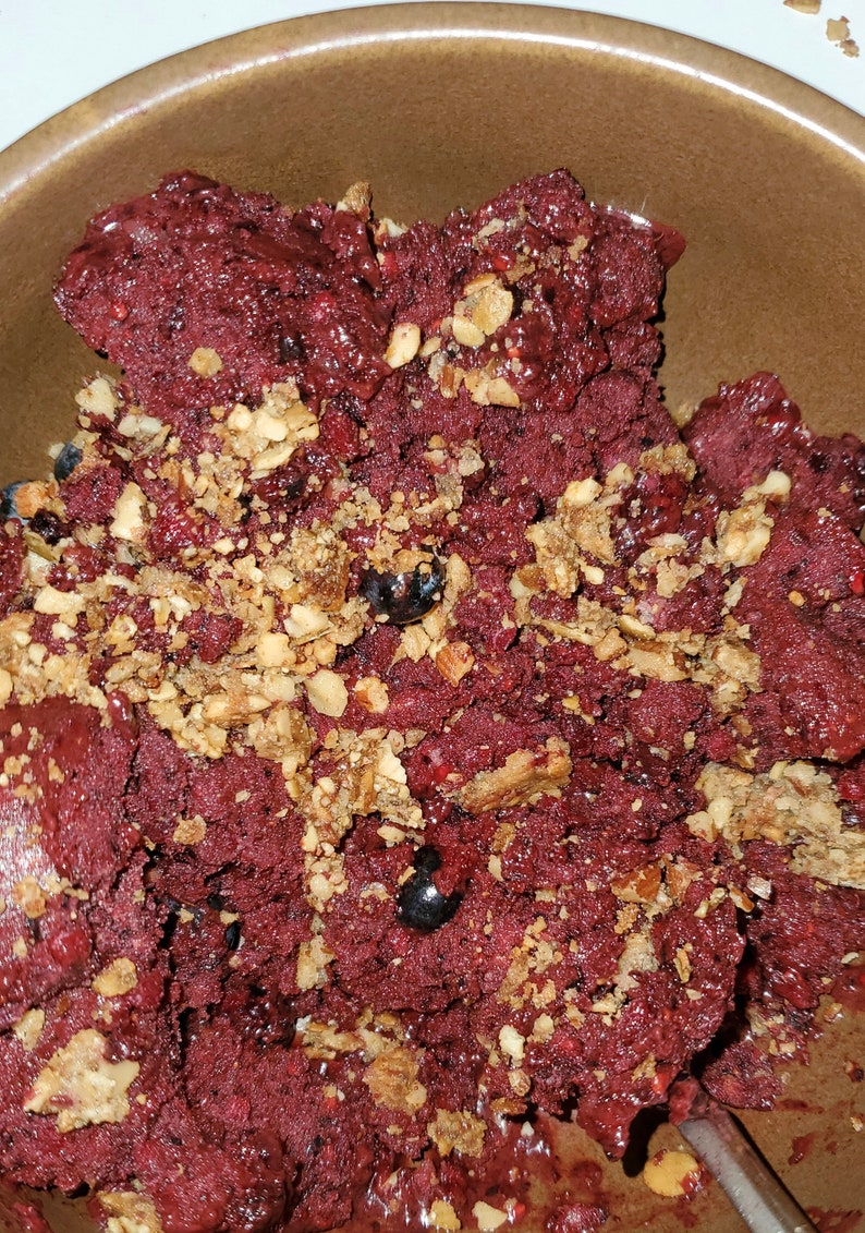 May include: A close-up of a bowl of red smoothie topped with granola and blueberries.