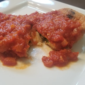 Peut inclure: Un chausson croustillant et doré, frit, rempli d'épinards et de fromage, coupé en deux et garni d'une sauce tomate rouge.