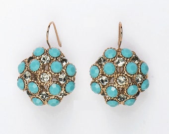 Puede incluir: Un par de pendientes dorados con un diseño de racimo. Cada pendiente presenta piedras facetadas de color azul claro y cristales transparentes engastados en un marco de metal dorado tejido. Los pendientes tienen un cierre de gancho.