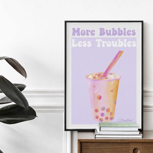Puede incluir: Una impresión enmarcada con un fondo morado y el texto "More Bubbles Less Troubles" en blanco. Una ilustración de dibujos animados de un vaso de té de burbujas rosa y naranja con una pajita y perlas de tapioca está en el centro de la impresión.
