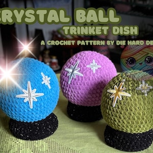 Puede incluir: Tres cuencos de adorno de bola de cristal de ganchillo en azul, morado y verde, cada uno con un adorno en forma de estrella. Las bases son negras y moteadas. El texto en la parte superior dice "CRYSTAL BALL TRINKET DISH". El texto en la parte inferior dice "A CROCHET PATTERN BY DIE HARD DESIGNS".