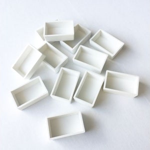 Può includere: Un set di 12 vaschette per acquerello in plastica bianca. Le vaschette sono disposte in modo casuale su una superficie bianca.
