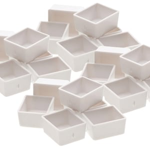Pode incluir: Um conjunto de 18 cubetas de tinta de aquarela de plástico branco. As cubetas estão dispostas em uma pilha aleatória.