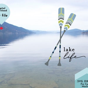 May include: Two crossed blue and yellow striped paddles with a lake scene in the background. The text "lake life" is written in a cursive font below the paddles.