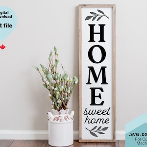 Könnte beinhalten: Ein Holzschild mit dem Wort "HOME" in schwarzen Buchstaben, gefolgt von den Worten "sweet home" in einer kursivschriftlichen Schriftart. Das Schild ist oben und unten mit grauen Blattwerk verziert. Das Schild befindet sich auf einem weißen Hintergrund.
