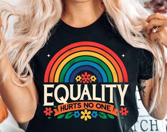 May include: A black t-shirt with a rainbow and the text "Equality Hurts No One". The rainbow is made up of red, orange, yellow, green, blue, indigo, and violet stripes. The text is in white with a black outline. The shirt is being worn by a person with long blonde hair.