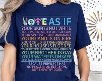 May include: Navy blue t-shirt with the text "VOTE AS IF" in colorful letters. The shirt's message continues with a list of social justice issues. The shirt is a crew neck and has short sleeves.