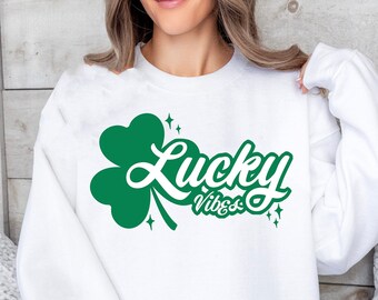May include: White sweatshirt with a green four-leaf clover and the text "Lucky Vibes" in a green cursive font.
