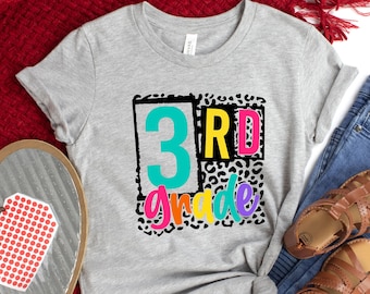 May include: A gray t-shirt with a black and white leopard print design. The text "3rd grade" is written in colorful letters on the shirt.
