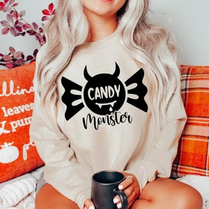 May include: A beige sweatshirt with a black graphic of a candy with horns and the text "Candy Monster".