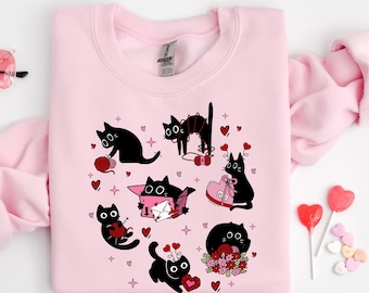 May include: A pink sweatshirt with a black cat design. The cats are holding hearts, yarn, and letters. The design is surrounded by small hearts and stars.