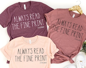 Puede incluir: Tres camisetas de diferentes colores con el texto "ALWAYS READ THE FINE PRINT I'M PREGNANT" impreso en ellas. Las camisetas están dispuestas sobre un fondo blanco.
