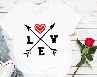 May include: White t-shirt with a black graphic design of two crossed arrows with a red heart in the center and the word "LOVE" in black letters.