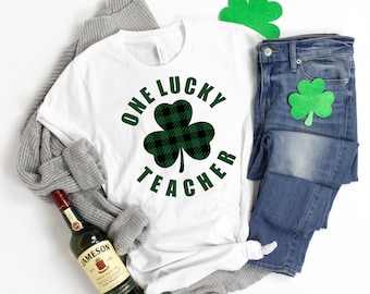 May include: White t-shirt with a green and black plaid shamrock and the text "One Lucky Teacher".