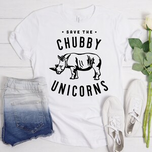 May include: White t-shirt with black text that reads "Save the Chubby Unicorns" and a black silhouette of a rhinoceros.