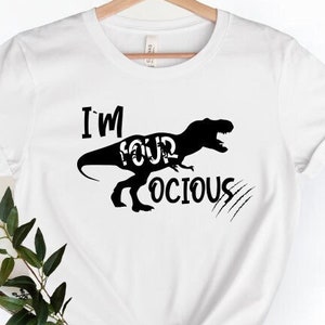 May include: White t-shirt with a black silhouette of a Tyrannosaurus Rex and the text "I'm Your  -ocious".