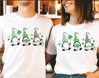 May include: Two white t-shirts with a graphic of three gnomes wearing green hats and holding shamrocks. The gnomes are wearing black and white striped pants.