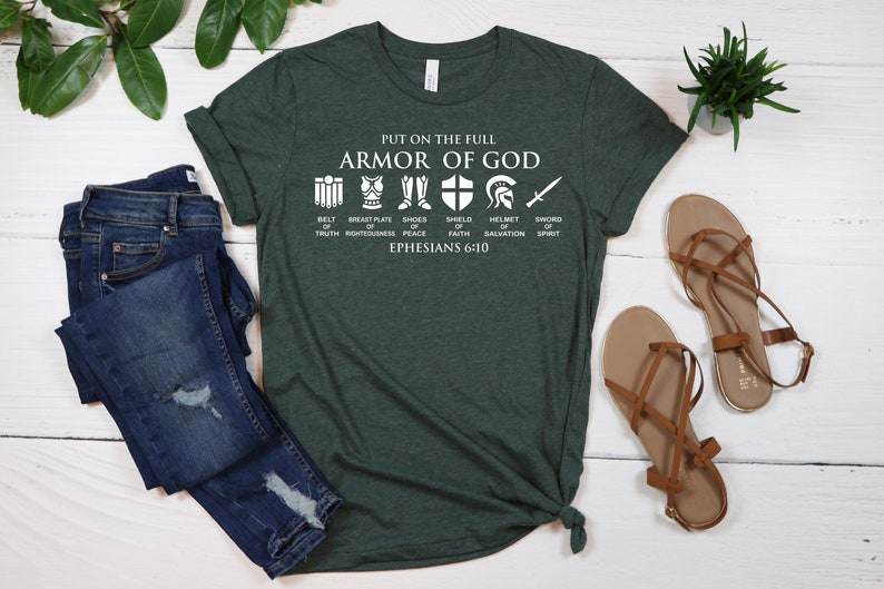 May include: A green t-shirt with a white graphic of the Armor of God. The graphic includes a belt, breastplate, shoes, shield, helmet, and sword. The text "PUT ON THE FULL ARMOR OF GOD" is above the graphic. The text "BELT OF TRUTH" is below the belt graphic. The text "BREASTPLATE OF RIGHTEOUSNESS" is below the breastplate graphic. The text "SHOES OF PEACE" is below the shoes graphic. The text "SHIELD OF FAITH" is below the shield graphic. The text "HELMET OF SALVATION" is below the helmet graphic. The text "SWORD OF SPIRIT" is below the sword graphic. The text "EPHESIANS 6:10" is below the graphic.