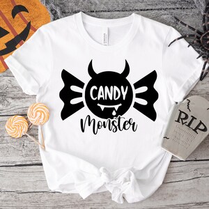 May include: White t-shirt with a black graphic of a candy with devil horns and the text "Candy Monster".