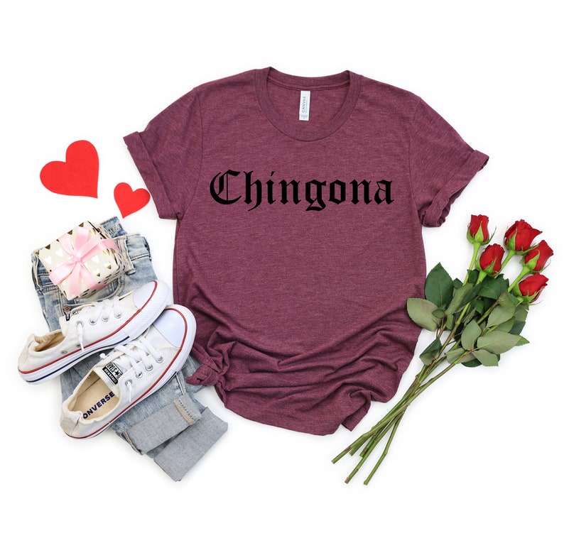 Op de afbeelding: Een maroon t-shirt met het woord "Chingona" gedrukt in zwarte gotische letters.