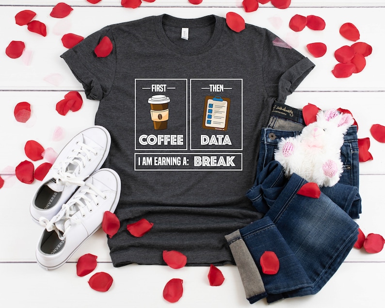 May include: A dark gray t-shirt with a white graphic design. The graphic features two boxes with the words "First" and "Then" above them. The first box shows a cup of coffee and the word "Coffee". The second box shows a checklist and the word "Data". Below the boxes is the text "I am earning a: Break".