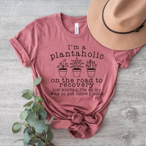 May include: A pink t-shirt with the text "I'm a plantaholic on the road to recovery just kidding, I'm on my way to get more plants".