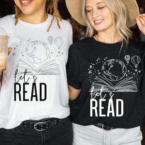 May include: Two people wearing black and white t-shirts with a graphic of a globe, a book, and the text "Let's Read".