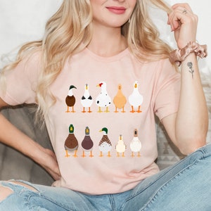 May include: A pink t-shirt with a graphic of nine different ducks in a row. The ducks are all facing forward and have different colors and patterns.