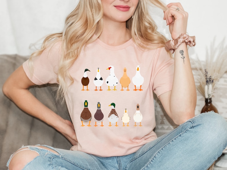 May include: A pink t-shirt with a graphic of nine different ducks in a row. The ducks are all facing forward and have different colors and patterns.