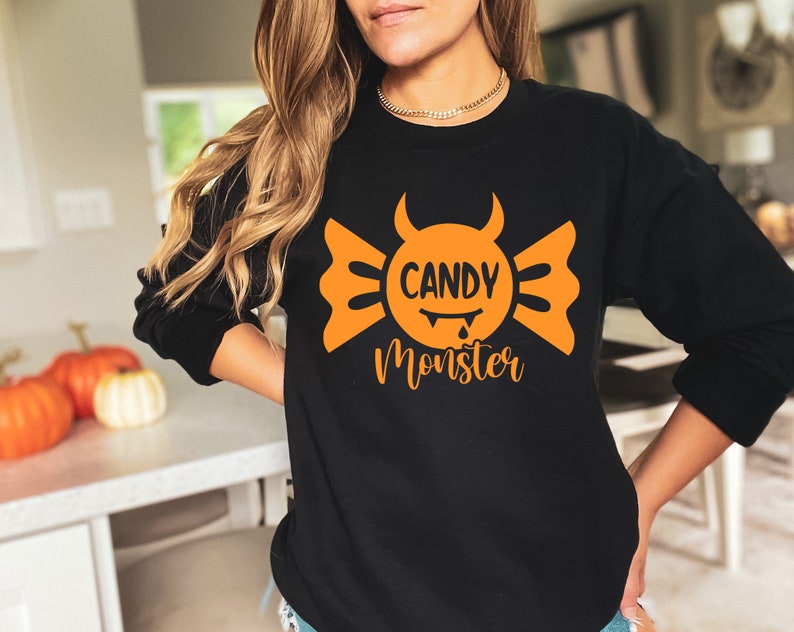May include: Black sweatshirt with an orange candy monster graphic. The graphic features a candy with a devil face and the text "Candy Monster".