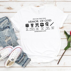 May include: White t-shirt with black text and icons that reads "Put on the full Armor of God." The icons represent the different parts of the armor: belt of truth, breastplate of righteousness, shoes of peace, shield of faith, helmet of salvation, and sword of the spirit. The text also includes "Ephesians 6:10".