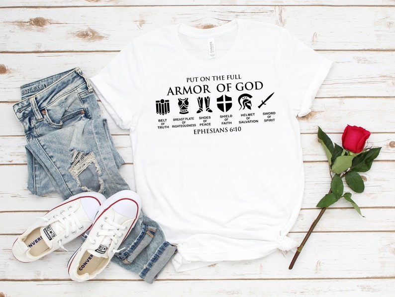May include: White t-shirt with black text and icons that reads "Put on the full Armor of God." The icons represent the different parts of the armor: belt of truth, breastplate of righteousness, shoes of peace, shield of faith, helmet of salvation, and sword of the spirit. The text also includes "Ephesians 6:10".