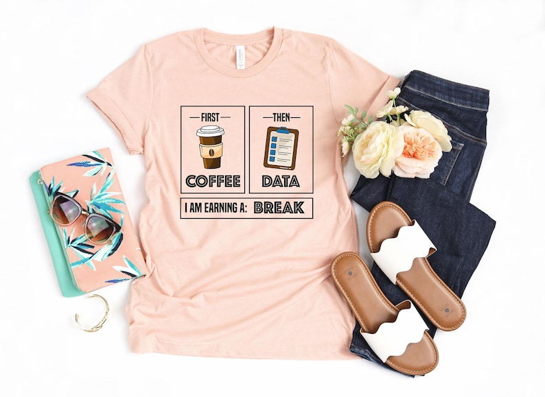 May include: A pink t-shirt with a graphic design that says "First Coffee, Then Data, I am earning a: Break". The graphic features a cup of coffee and a clipboard with a checklist.