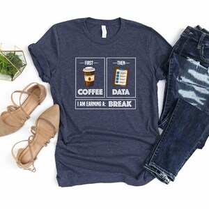 May include: A navy blue t-shirt with a white graphic that says "First - Coffee, Then - Data, I am earning a: Break". The graphic includes a cartoon image of a cup of coffee and a clipboard.