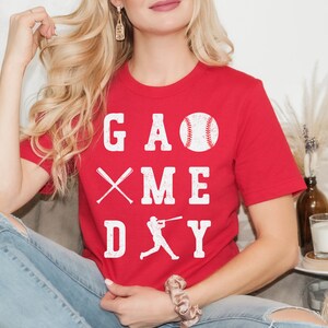 May include: Red t-shirt with a white graphic that says "GAME DAY" with a baseball, bats, and a baseball player silhouette.