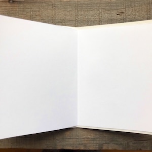 May include: Blank white card with a white envelope. The card is folded in half and the envelope is lying on top of the card.