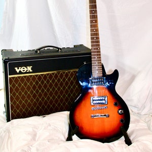 May include: A black and brown electric guitar with a sunburst finish and a black amplifier with a brown grill and the word "VOX" in gold lettering.