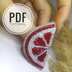 May include: A red and white beaded fruit slice brooch with a rhinestone in the center. The brooch is held in a hand with a white background.  PDF TUTORIAL is written in a circle in the upper left corner of the image.