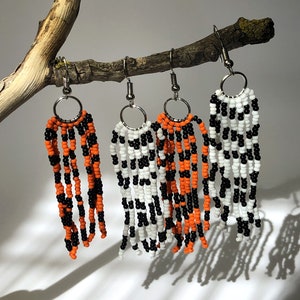 May include: Three pairs of dangle earrings with black, white, and orange beads. The earrings are hanging from a branch.