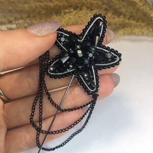 May include: A black beaded starfish brooch with a silver chain attached to a black pin.