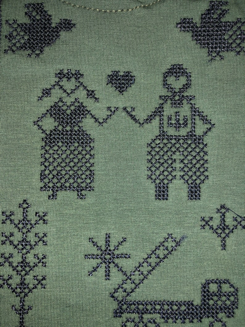 May include: Green fabric with a black embroidered design of two figures holding hands, a heart, and various other geometric shapes.