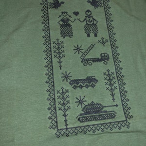 May include: Green t-shirt with a black embroidered design. The design features a couple, trees, a truck, a tank, and a snowflake.
