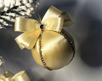Puede incluir: Un adorno de Navidad de satén amarillo pálido con un gran lazo y un borde de strass.