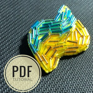 May include: A yellow felt shape covered in blue and gold seed beads. The shape is reminiscent of a stylized heart. The image includes the text "PDF TUTORIAL".