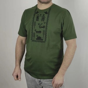 May include: A green short-sleeved t-shirt with a black embroidered design featuring a couple, a truck, a star, and a tank.