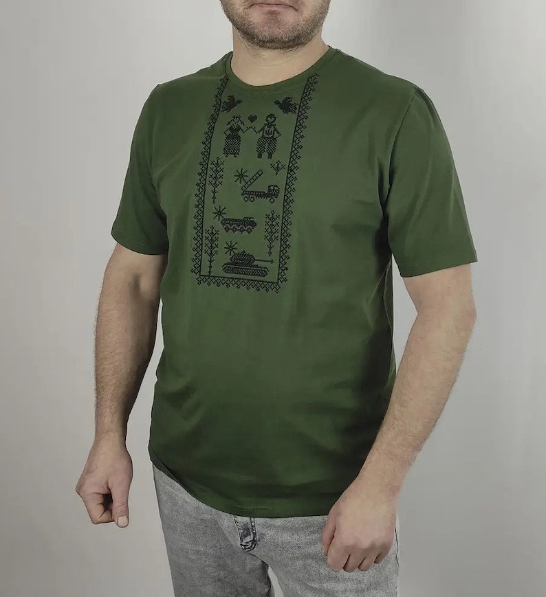 May include: A green short-sleeved t-shirt with a black embroidered design featuring a couple, a truck, a star, and a tank.