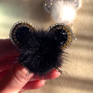 May include: Black faux fur pom-pom with black and gold beaded ears. The pom-pom is attached to a gold chain.