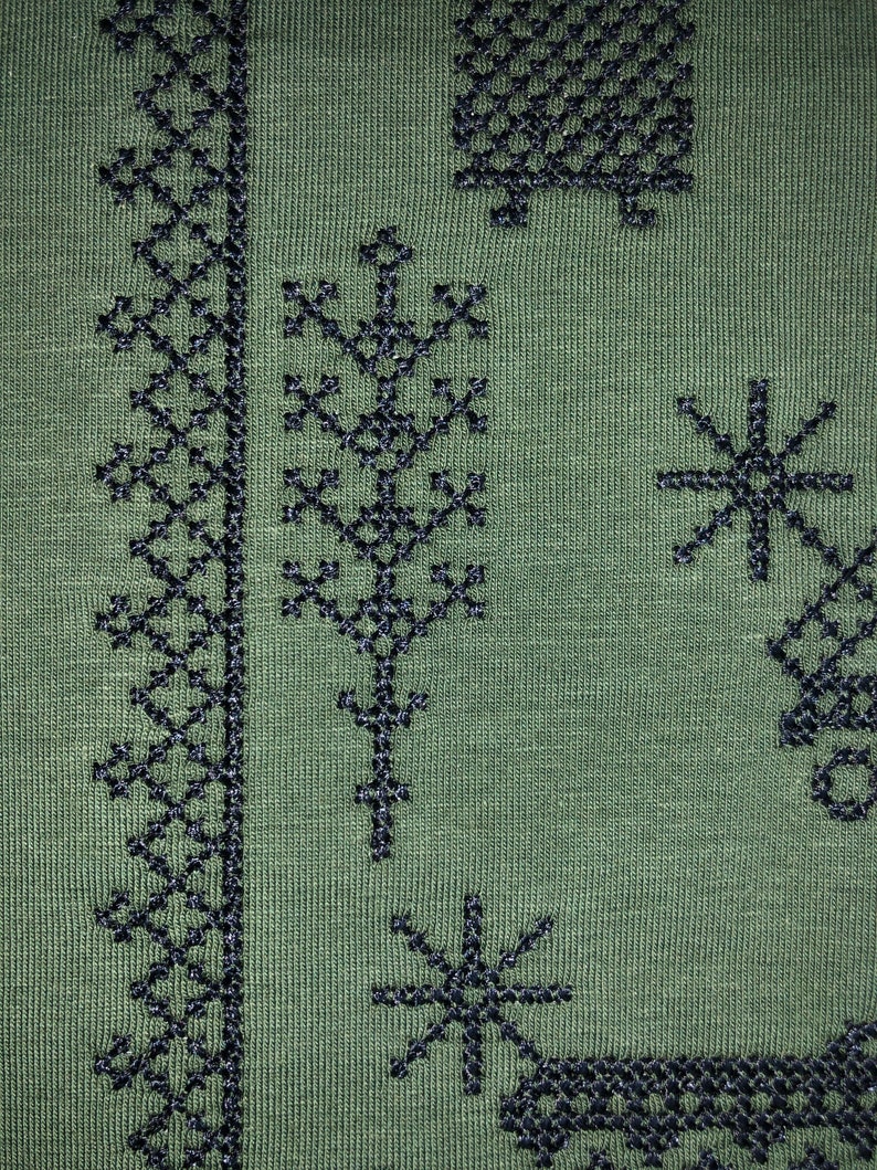 May include: Green fabric with black embroidered designs. The designs include a repeating pattern of geometric shapes, a tree, and stars.