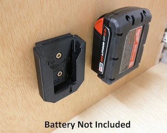 May include: A black plastic wall mount for a Milwaukee M18 Red Lithium CP2.0 battery. The mount has two screws and the text "For Milwaukee" is visible. Battery not included.