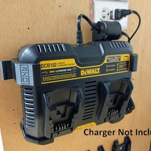 Puede incluir: Una estación de carga DeWalt DCB102 Jobsite negra y amarilla con un puerto USB y un soporte de pared negro. El texto "Cargador no incluido" está impreso en la superficie de madera debajo del cargador.